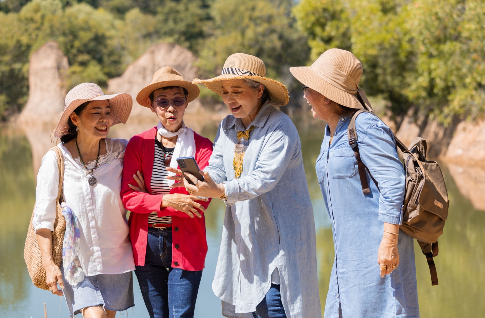 A group of senior friends gather around a phone for trail advice while walking outdoors in a local park