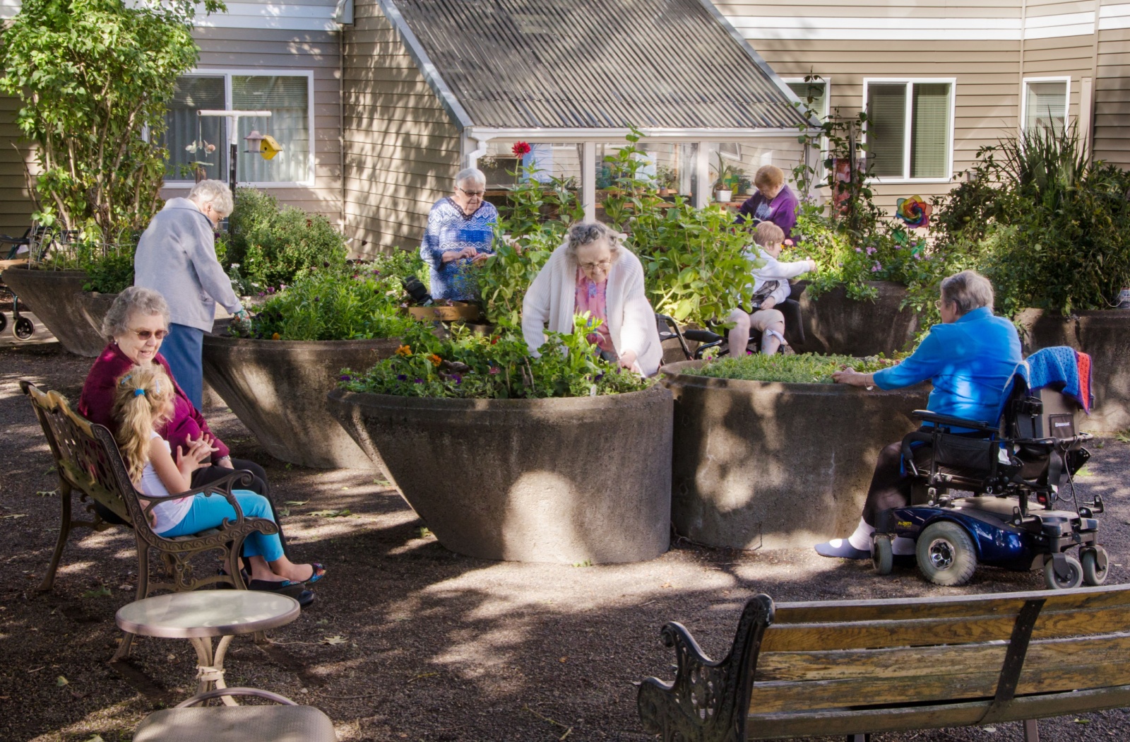 A group of seniors in assisted living spend time outdoors in the community gardens, enjoying the outdoors and sunshine
