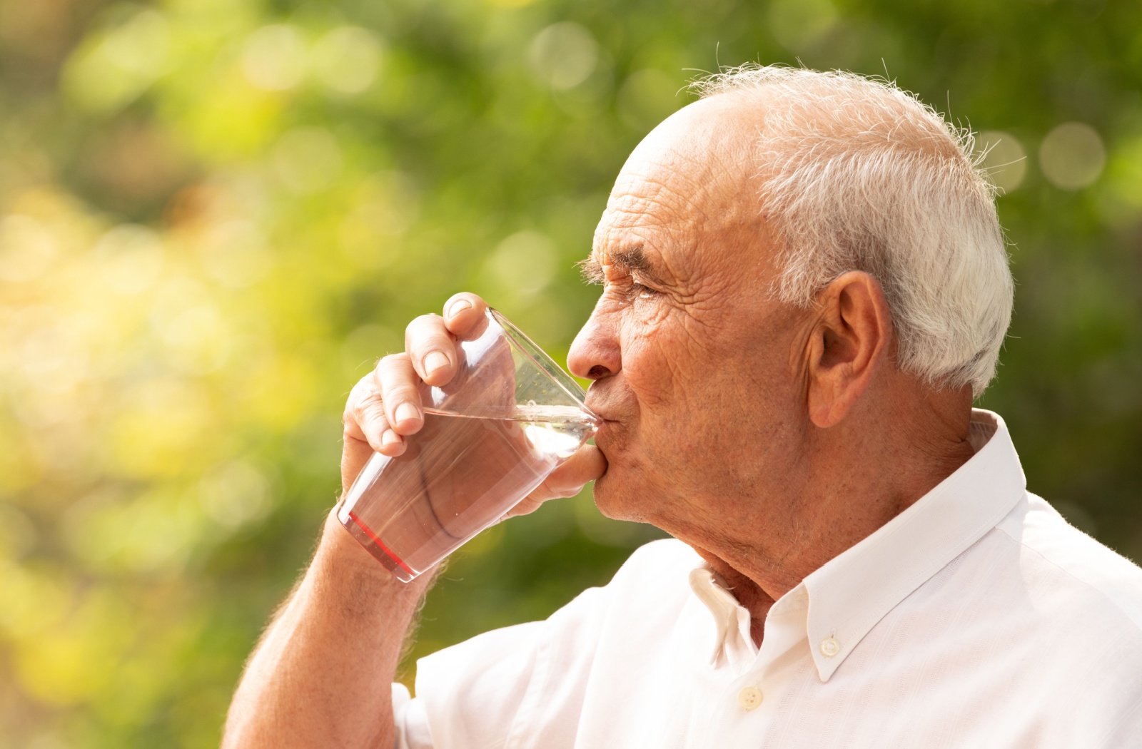 A senior drinks a class of water outside.