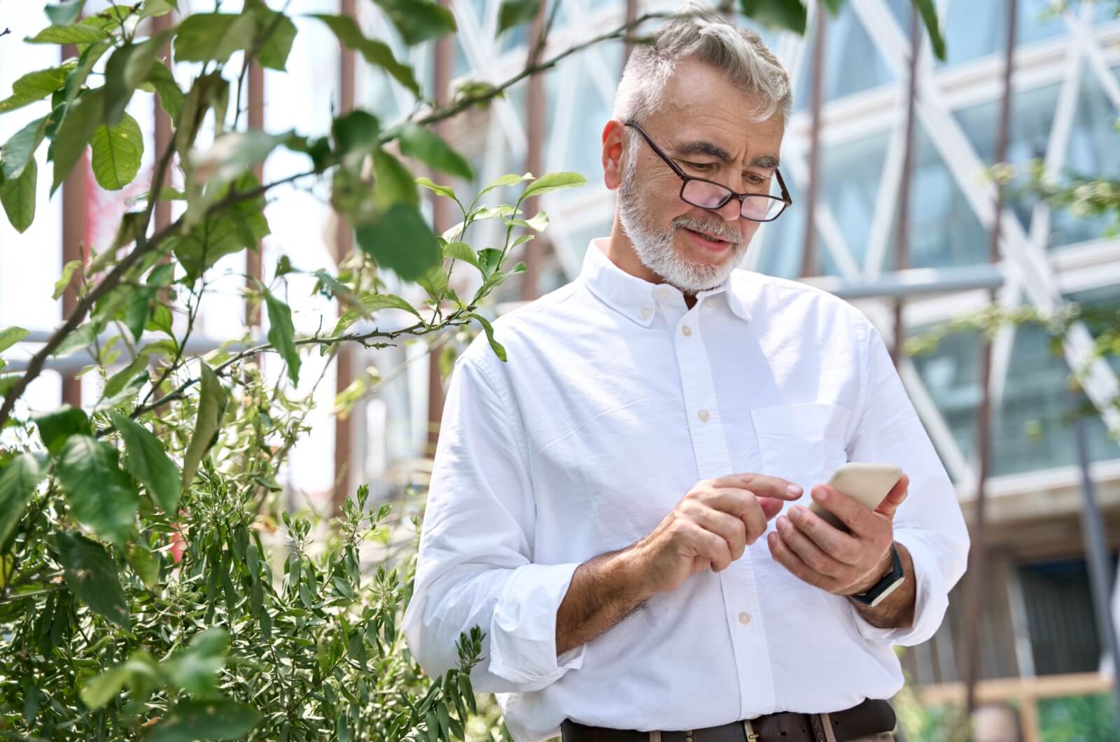 Older man standing in a park in the city and using an app on his smartphone