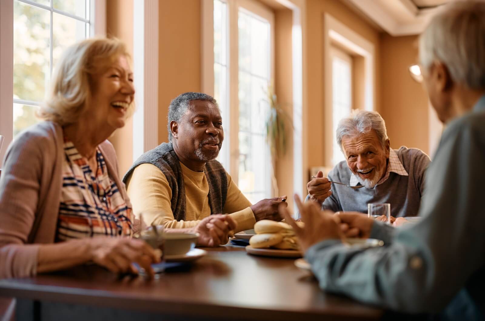 A group of older adults around the table in senior living, smiling and talking while enjoying a denture-friendly breakfast.