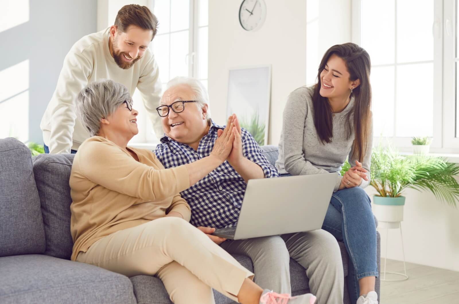 An adult couple helps their senior parents make plans for a short-term stay in a respite care community on the computer.