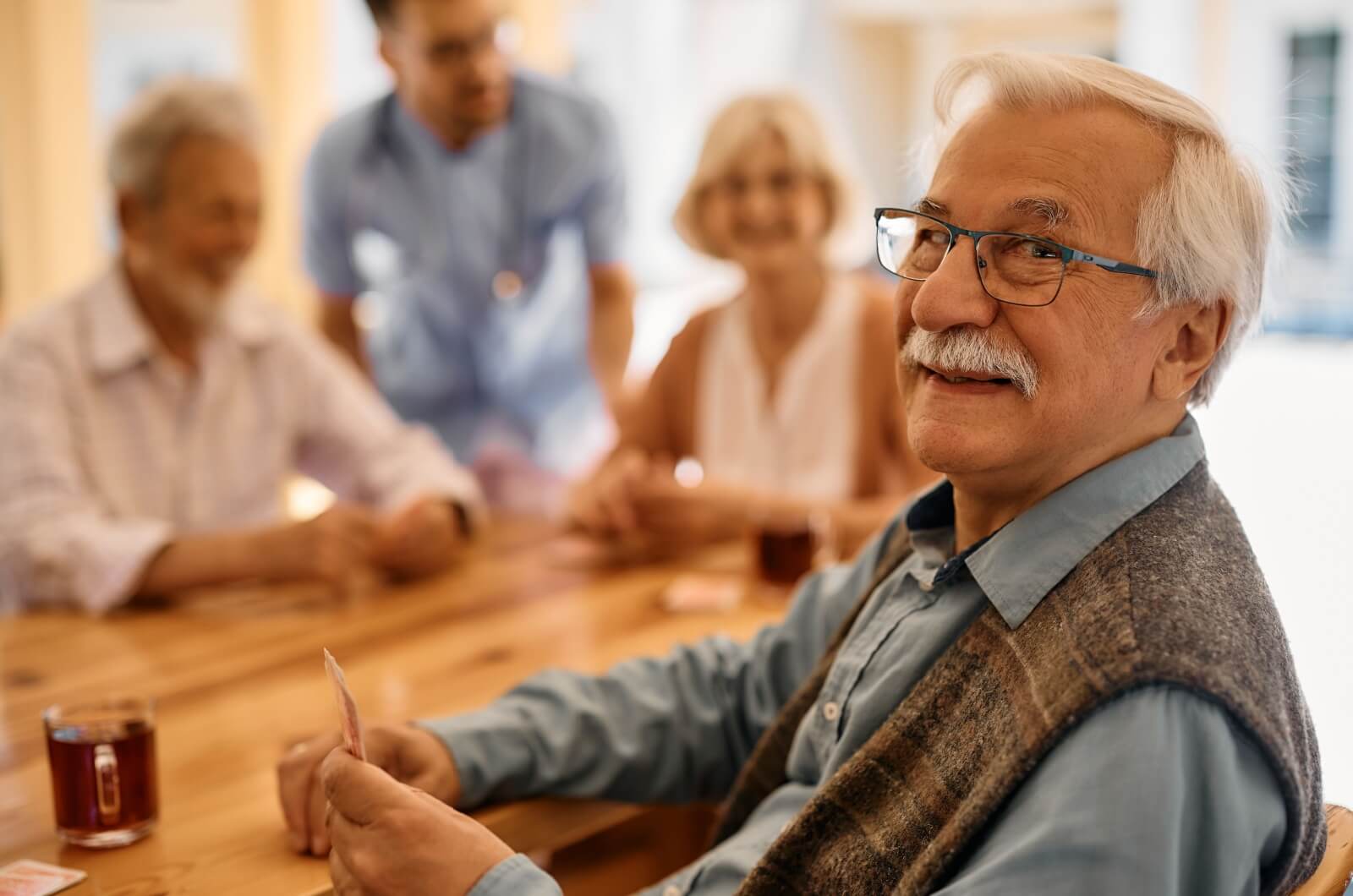 An older adult smiling and looking at the camera during a friendly game of cards in a retirement home.