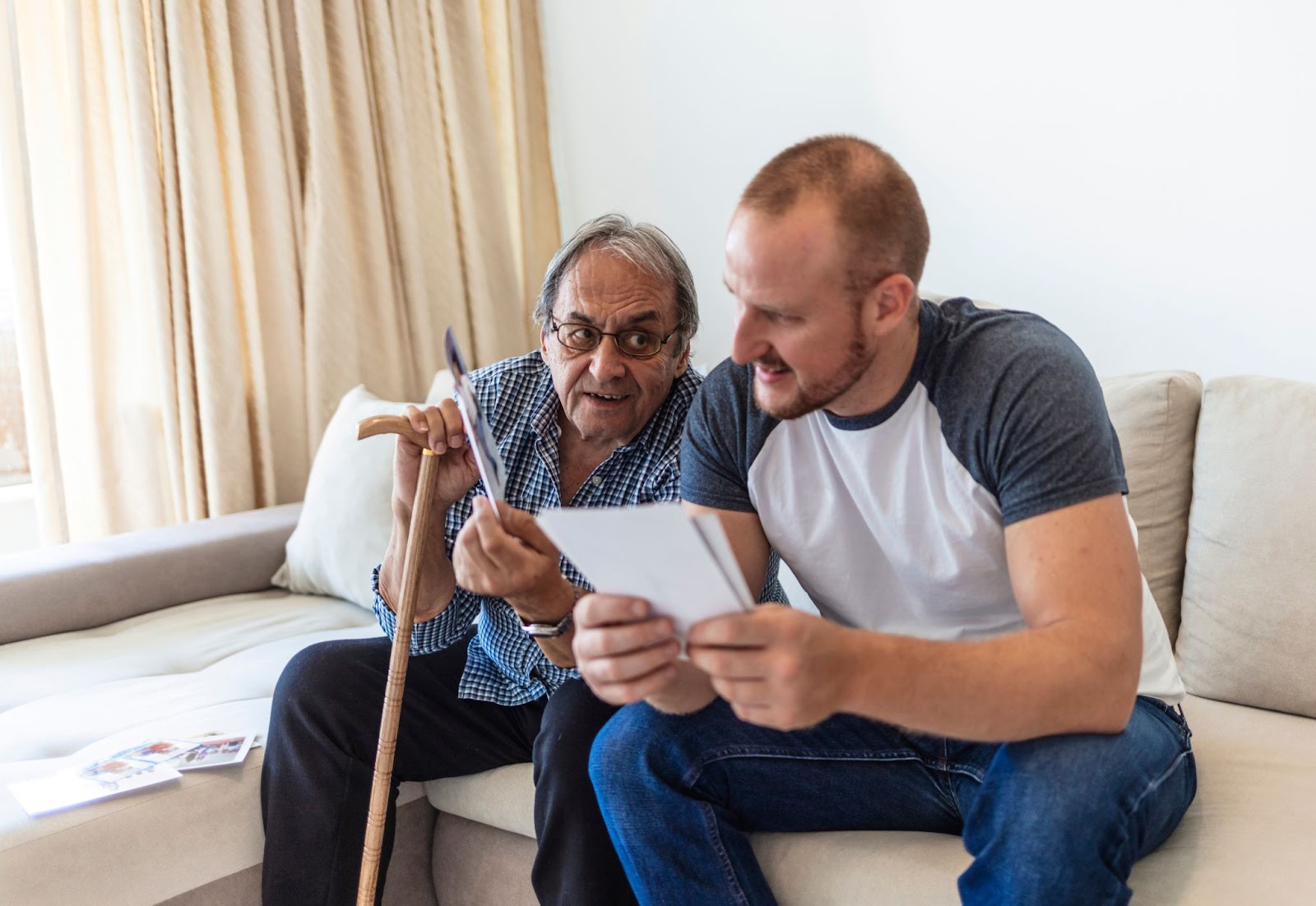 A senior and his adult son reminisce together over photographs.