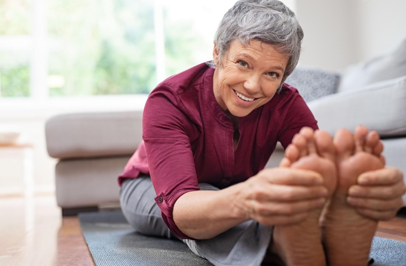 An older adult woman doing toe exercise while sitting on a yoga mat.