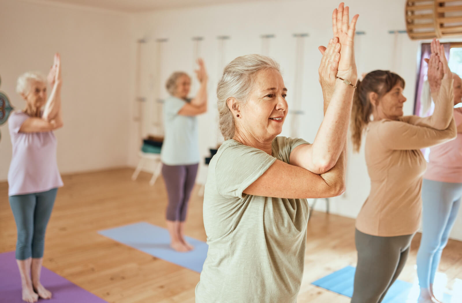 Elderly individuals gracefully perform standing yoga exercises on their mats, fostering strength and balance.