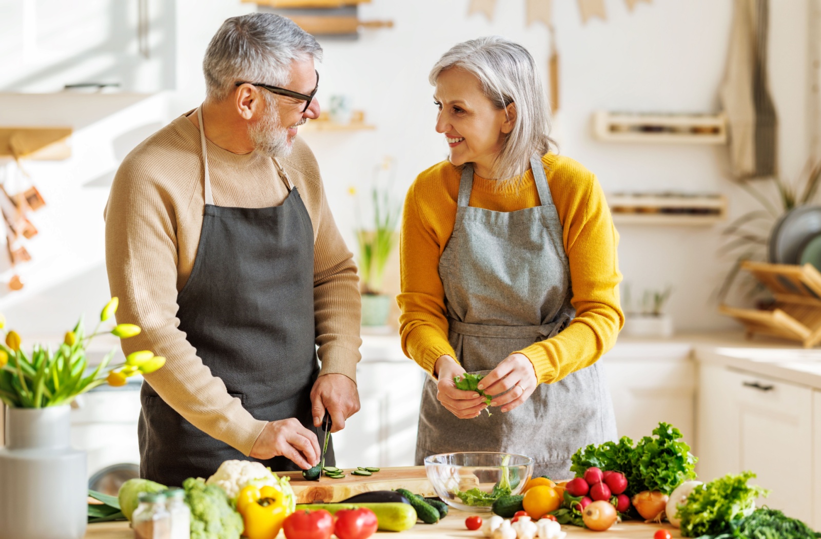 An older couple smiling at one another in their kitchen while making a heart-healthy salad.